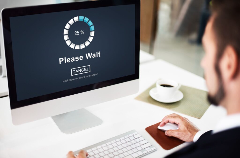 Man at a desk viewing a computer screen showing a "Please Wait" loading circle at 25%.
