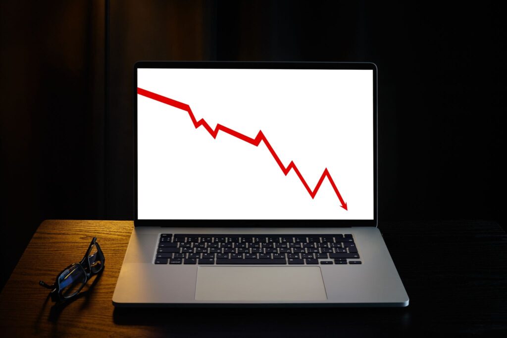 Laptop screen displaying a red downward-trending line graph, with glasses resting beside it on a desk
