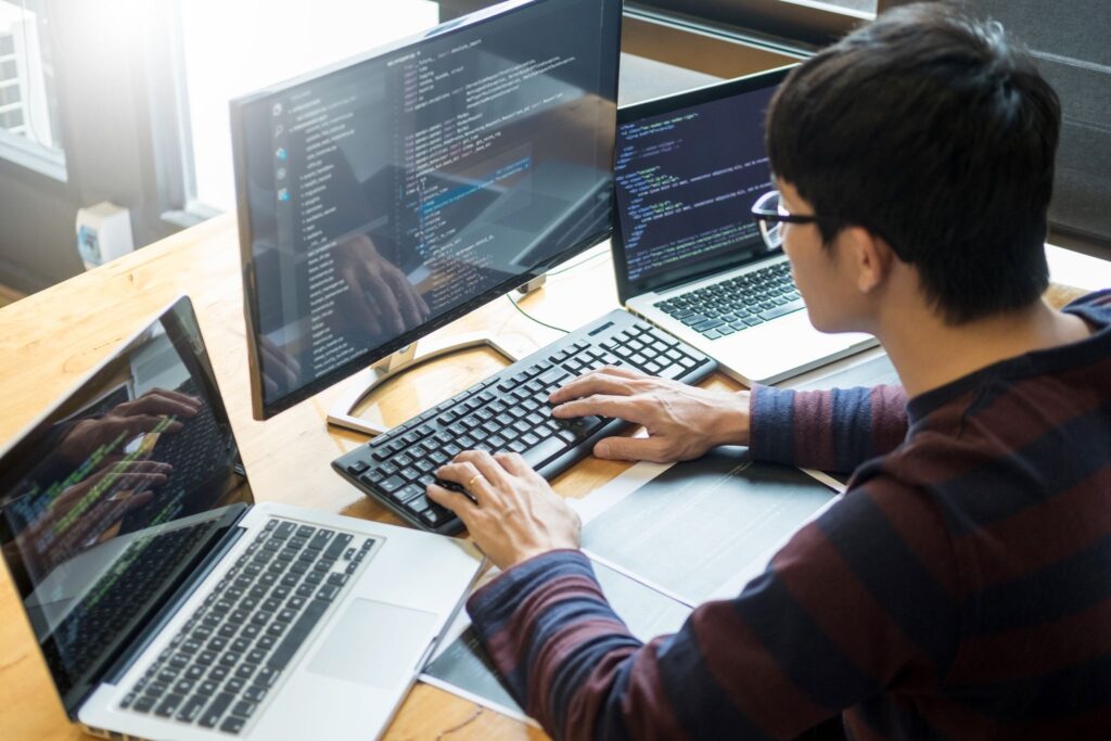 Programmer typing code across multiple laptops and a monitor