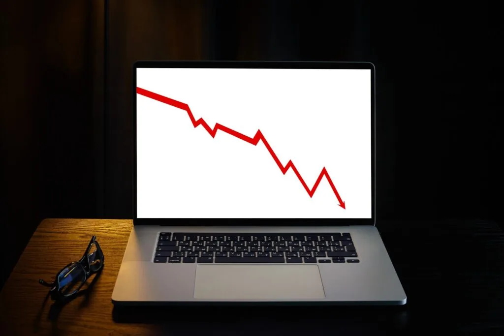 Laptop screen displaying a red downward-trending line graph, with glasses resting beside it on a desk